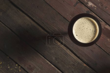 Photo for Top view of a glass of cold dark beer placed on a rustic wooden table - Royalty Free Image
