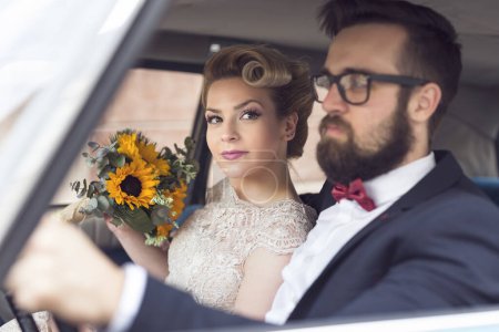 Téléchargez les photos : Jeune couple de jeunes mariés assis dans une voiture vintage rétro, partir en lune de miel. Focus sur la mariée - en image libre de droit