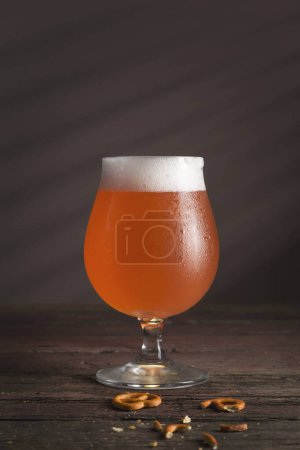 Téléchargez les photos : Verre de bière au pamplemousse rouge froid et quelques bretzels sur une table rustique en bois - en image libre de droit