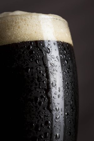 Foto de Primer plano de un vaso húmedo de cerveza fría oscura con espuma. Enfoque selectivo - Imagen libre de derechos