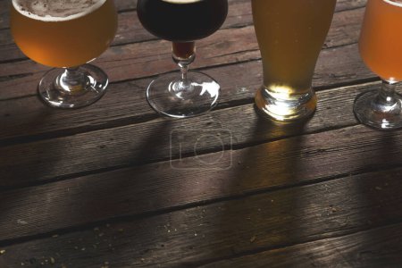Téléchargez les photos : Détail de la bière pâle, foncée, non filtrée et aux fruits rouges dans quatre verres à bière différents sur une table en bois rustique. - en image libre de droit