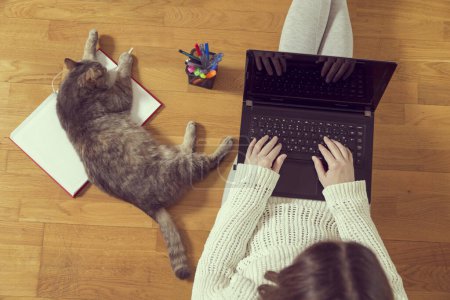 Foto de Vista superior de una mujer trabajando en su portátil en casa con su gato como asistente. Enfoque selectivo - Imagen libre de derechos
