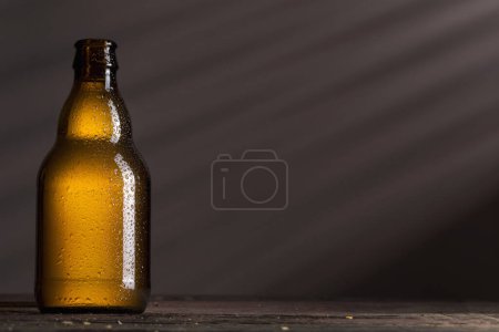 Téléchargez les photos : Bouteille de bière humide bien refroidie placée sur une table en bois rustique dans un bar - en image libre de droit