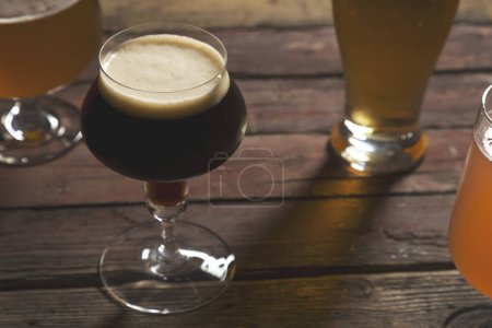 Photo for Pale, dark, unfiltered pale and red fruit beer in four different beer glasses on a rustic wooden table. Selective focus on the foam - Royalty Free Image