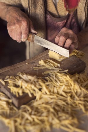 Téléchargez les photos : Détail des nouilles coupées à la main d'une femme âgée avec un vieux couteau lors de la fabrication de pâtes maison. Concentration sélective - en image libre de droit