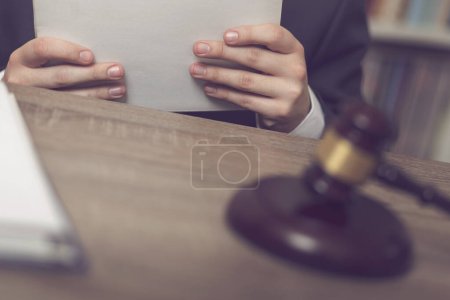 Téléchargez les photos : Détail d'un juge assis à son bureau, tenant un dossier avec une nouvelle affaire et l'étudiant. Concentration sélective - en image libre de droit