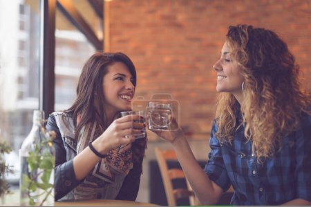 Foto de Dos chicas sentadas en un café, bebiendo agua de desintoxicación con hojas de menta y divirtiéndose. Concéntrate en la chica de la izquierda - Imagen libre de derechos