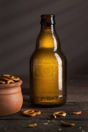 Foto de Botella de cerveza fría pálida con un tazón de pretzels colocado en una mesa de madera rústica - Imagen libre de derechos