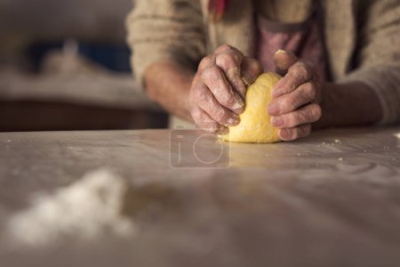 Foto de Detalle de la mano de una anciana amasando masa mientras hace pasta casera. Enfoque selectivo - Imagen libre de derechos
