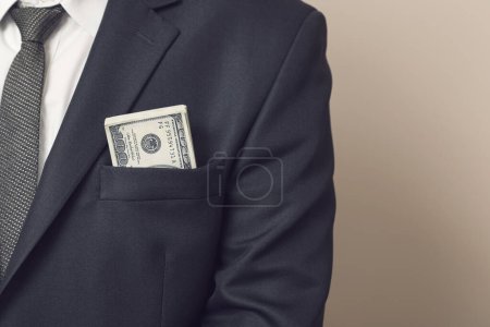 Téléchargez les photos : Détail d'un homme d'affaires en costume avec des billets de cent dollars dans la poche de sa veste. Concentration sélective - en image libre de droit