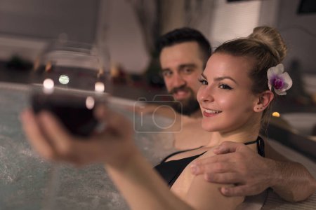 Photo for Couple in love enjoying the romantic atmosphere of a jacuzzi bath, drinking wine and relaxing - Royalty Free Image