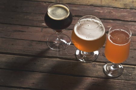 Foto de Cerveza de fruta pálida, oscura y roja en tres vasos de cerveza diferentes sobre una mesa de madera rústica. Enfoque selectivo - Imagen libre de derechos