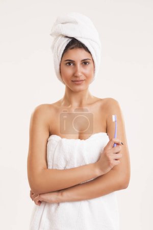 Foto de Hermosa joven envuelta en toallas de algodón blanco después de tomar un baño, sosteniendo un cepillo de dientes - Imagen libre de derechos