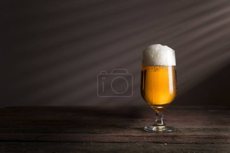 Foto de Vaso de cerveza fría y pálida colocado sobre una mesa rústica de madera - Imagen libre de derechos