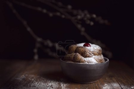 Photo for Marble cake sprinkled with powdered sugar with a cherry fruit on the top, placed in a bowl on a rustic wooden table. Selective focus - Royalty Free Image