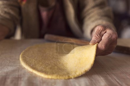 Photo for Detail of an elderly woman's hand holding a rolled out dough while making homemade pasta. Selective focus - Royalty Free Image