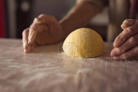 Foto de Detalle de la mano de una anciana amasando masa mientras hace pasta casera. Enfoque selectivo - Imagen libre de derechos