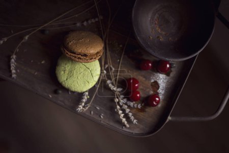 Photo for Top view of macaron cookies on a wooden tray, with a bowl, cherry fruit and lavender flowers placed next to it. Selective focus - Royalty Free Image