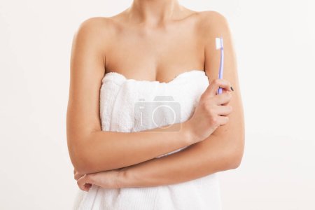 Téléchargez les photos : Détail d'une belle jeune femme enveloppée dans des serviettes en coton blanc après avoir pris un bain, tenant une brosse à dents - en image libre de droit