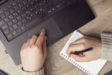 Foto de Vista superior de manos masculinas escribiendo en una computadora portátil y tomando notas - Imagen libre de derechos