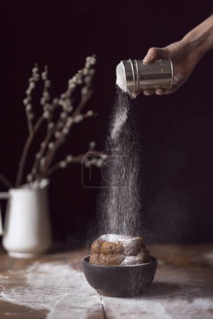 Photo for Detail of female hand sprinkling marble cake placed on a rustic wooden table with powdered sugar. Selective focus - Royalty Free Image