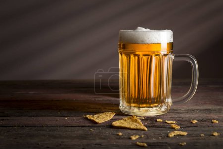 Photo for Mug of cold pale beer placed on a burlap cover with some tortilla chips on a rustic wooden table. Selective focus - Royalty Free Image