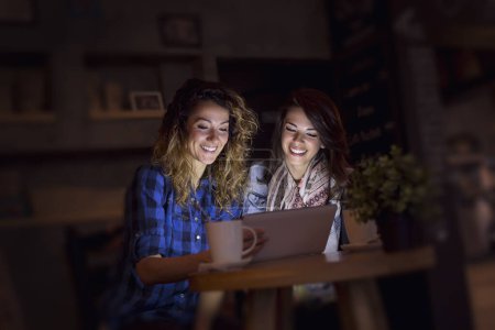 Téléchargez les photos : Deux amis assis dans un café, surfant sur le net sur une tablette et postant sur les réseaux sociaux - en image libre de droit