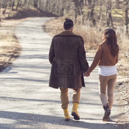 Téléchargez les photos : Couple tenant la main et marchant sur la route à travers une forêt, profitant d'une journée de printemps ensoleillée - en image libre de droit