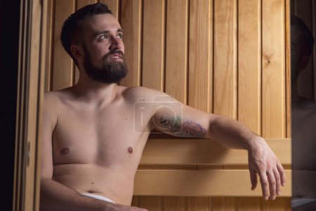 Téléchargez les photos : Beau jeune homme relaxant et profitant d'une séance de sauna finlandaise - en image libre de droit