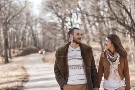 Téléchargez les photos : Couple tenant la main et marchant sur la route à travers une forêt, profitant d'une journée d'automne ensoleillée - en image libre de droit