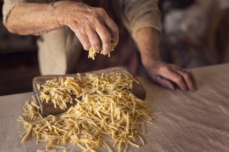 Téléchargez les photos : Détail de la main d'une femme âgée tenant une poignée de nouilles tout en faisant des pâtes maison. Concentration sélective - en image libre de droit