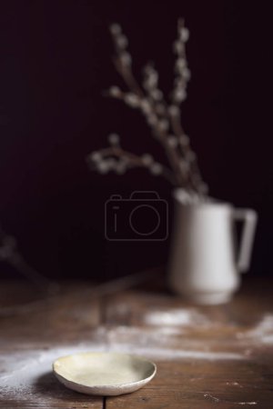 Photo for Rustic plate placed on a wooden table sprinkled with flour with a flower vase in the background. Selective focus on the plate - Royalty Free Image
