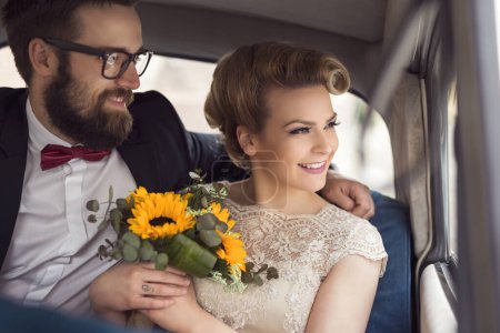 Photo for Young newlywed couple sitting in a retro vintage car, hugging and going away on a honeymoon - Royalty Free Image