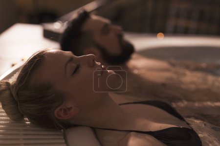 Photo for Couple enjoying and relaxing in a jacuzzi bath with warm water, bubbles and candle light. Focus on the girl's nose and lips - Royalty Free Image