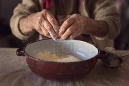 Téléchargez les photos : Détail de la main d'une femme âgée écrasant un oeuf et le mettant dans la farine tout en faisant des pâtes maison. Concentration sélective - en image libre de droit