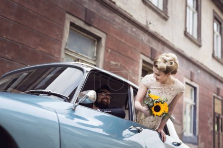 Foto de Joven pareja de recién casados en un coche retro vintage, novio de conducción mientras la novia está saludando a través de una ventana mientras se van en su luna de miel. Concéntrate en la novia - Imagen libre de derechos