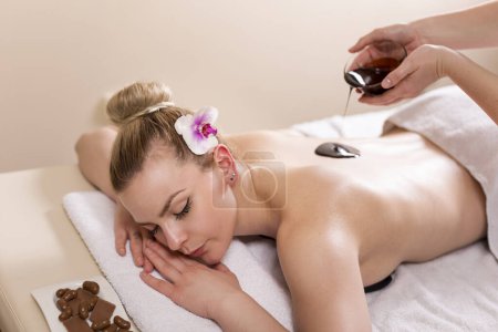 Téléchargez les photos : Femme couchée dans un salon de beauté, profitant d'un massage relaxant du dos avec du chocolat - en image libre de droit