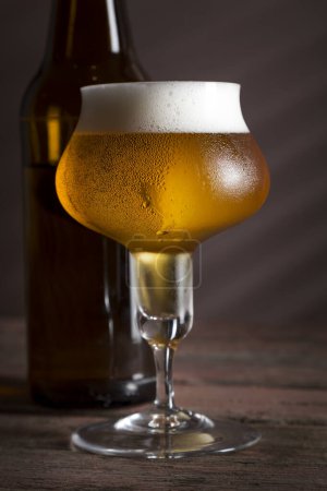Foto de Botella de cerveza y una taza de cerveza fría y pálida colocada en una mesa de madera rústica. Enfoque selectivo - Imagen libre de derechos