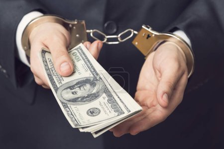 Photo for Businessman in a suit with handcuffs, arrested, offering bribery money for his release. Selective focus - Royalty Free Image