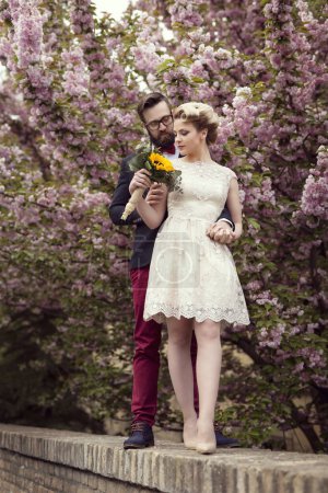 Photo for Newlywed couple standing in the street next to a cherry blossom tree, hugging and holding a sunflower wedding bouquet - Royalty Free Image