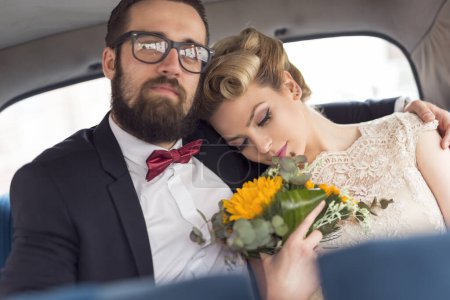 Foto de Joven pareja recién casada sentada en un coche retro vintage, abrazándose y marchándose de luna de miel. Concéntrate en la novia - Imagen libre de derechos