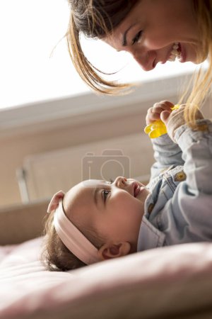 Foto de Joven madre acostada en la cama, sonriendo y jugando con su bebé. Concéntrate en el bebé - Imagen libre de derechos