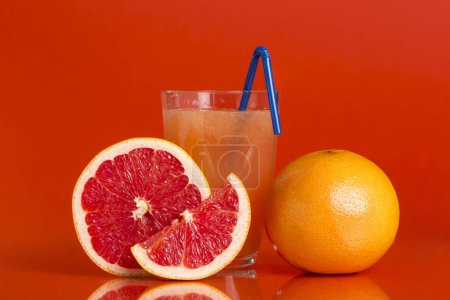 Photo for Whole red grapefruit, cross section and a slice placed next to a glass of grapefruit juice with drinking straw isolated on red background. Focus stacked image - Royalty Free Image