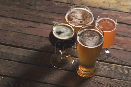 Photo for Pale, dark, unfiltered pale and red fruit beer in four different beer glasses on a rustic wooden table. Selective focus - Royalty Free Image