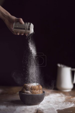 Photo for Detail of female hand sprinkling marble cake placed on a rustic wooden table with powdered sugar. Selective focus - Royalty Free Image
