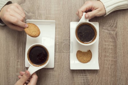 Téléchargez les photos : Vue du dessus des mains masculines et féminines tenant des tasses de café américain avec plaque de biscuits aux pépites de chocolat placés à côté - en image libre de droit