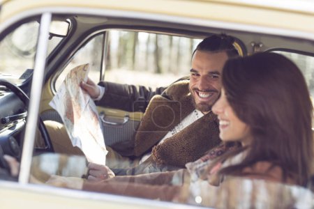 Téléchargez les photos : Jeune couple s'amuser et profiter d'un road trip. Fille conduisant une voiture pendant que le gars est assis et regardant la carte - en image libre de droit