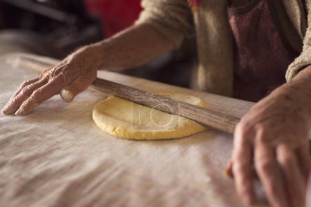 Photo for Detail of an elderly woman's hand rolling out a dough with a rolling pin while making homemade pasta. Selective focus - Royalty Free Image
