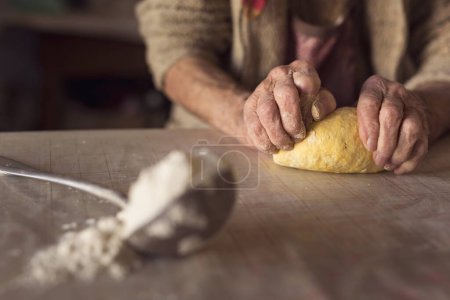 Téléchargez les photos : Détail de la main d'une femme âgée pétrissant la pâte tout en faisant des pâtes maison. Concentration sélective - en image libre de droit