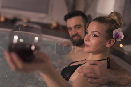 Téléchargez les photos : Couple amoureux profiter de l'atmosphère romantique d'une baignoire jacuzzi, boire du vin et se détendre. Escapade spa romantique - en image libre de droit
